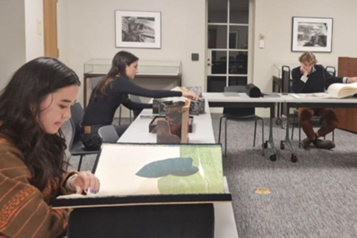 Image of students sitting at desks looking through large artists’ books.