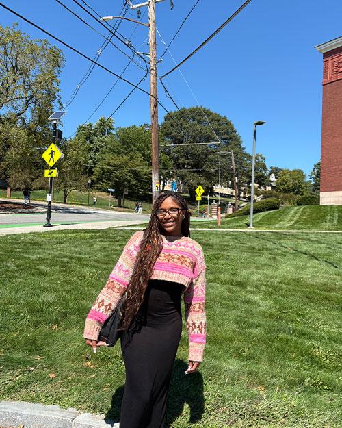 Jazmyne Garrett smiling by a grassy hill in a colorful sweater and black dress