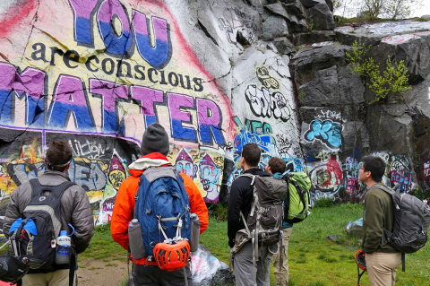 Group of backpackers looking at grafitti-covered rock.