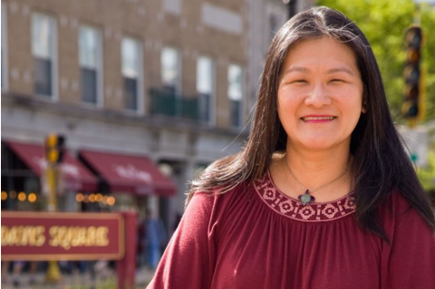Fannie Koa posing in Davis Square, smiling at the camera. She has long, straight, black hair and is wearing a red top.