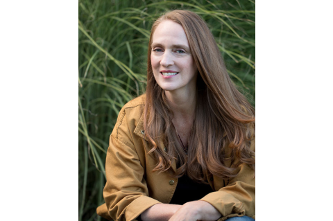 Image of Julie Carrick Dalton sitting amongst green reeds, smiling at the camera. She has long blonde hair and is wearing a yellow jacket.