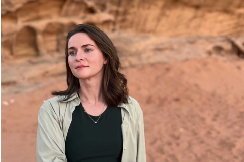 Woman in green shirt standing in the desert, looking away from the camera